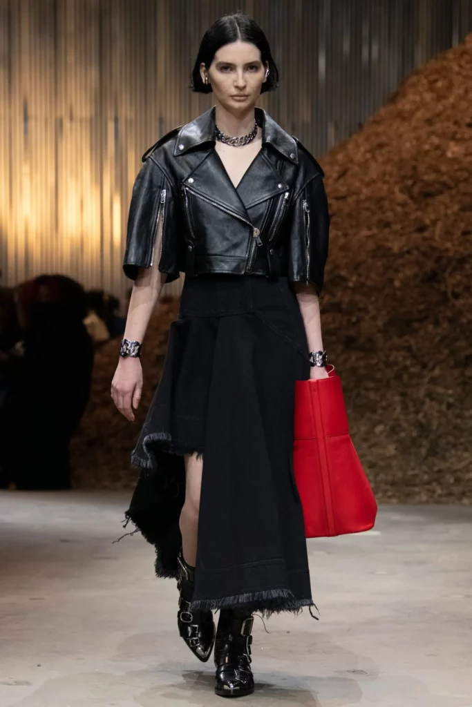 Runway model in Alexander McQueen leather jacket, black skirt, and red bag